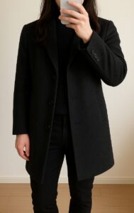 黒のウールチェスターコートを着た人物の室内自撮り。厚くて硬い生地が肩の角に乗り、肩幅と胸まわりが大きく見えている例。