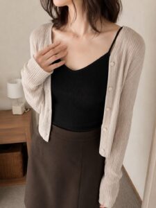 黒いキャミソールとベージュのカーディガン姿で鎖骨の下へ片手を添えた女装男子の上半身写真