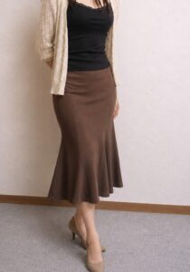 身体を少し斜めにし、片足に体重を乗せて立つ茶色のマーメイドスカート姿の女装男子