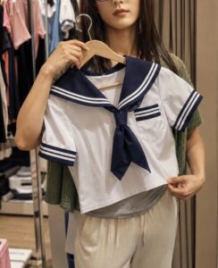 白地に紺の襟と袖ラインが入ったセーラー服をハンガーに掛け、体の前で持って確認する女装男子